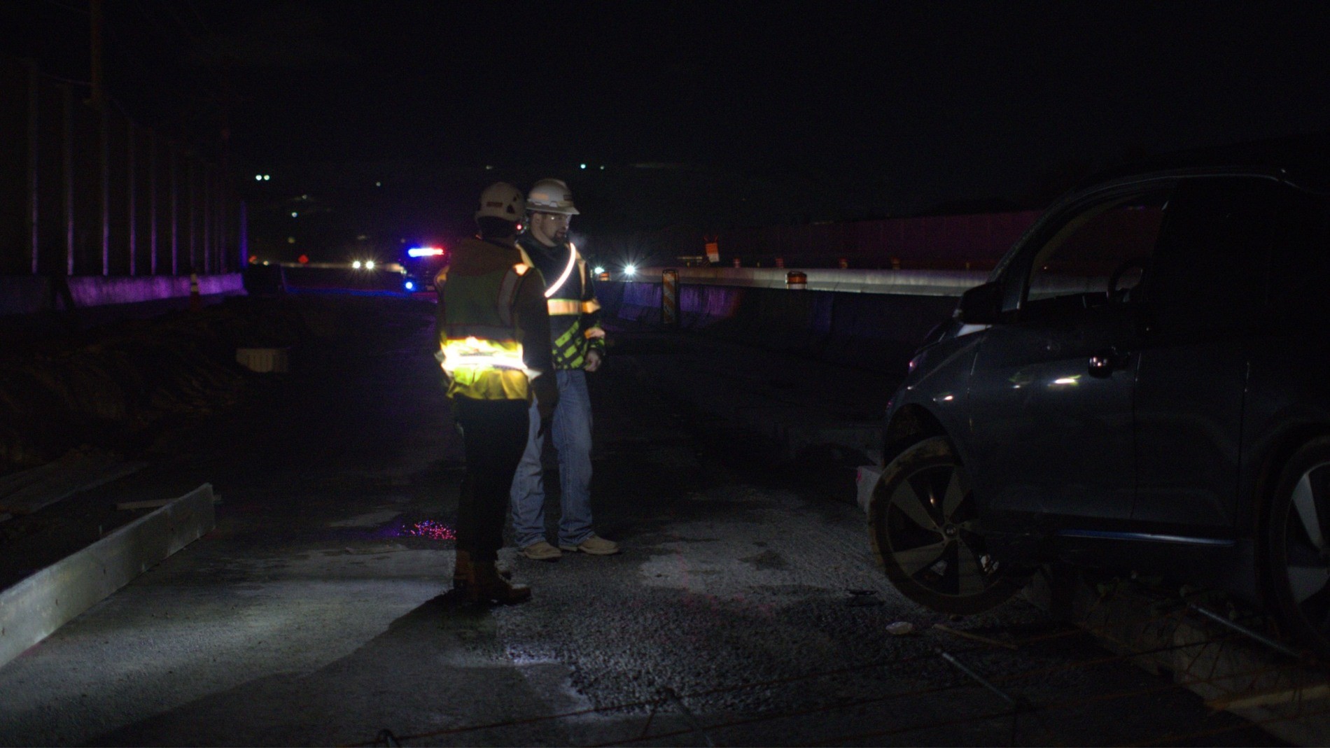 Workers wearing illuminated belts alongside vehicles on a nighttime construction site