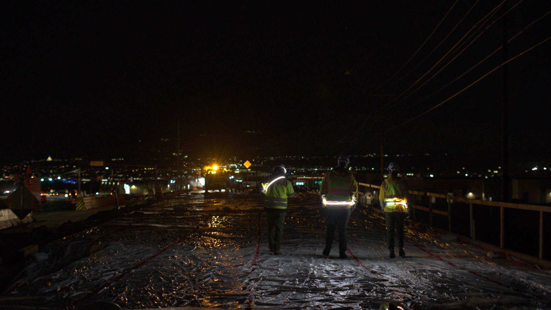 Three workers wearing illuminated Orion belts at an active construction site at night